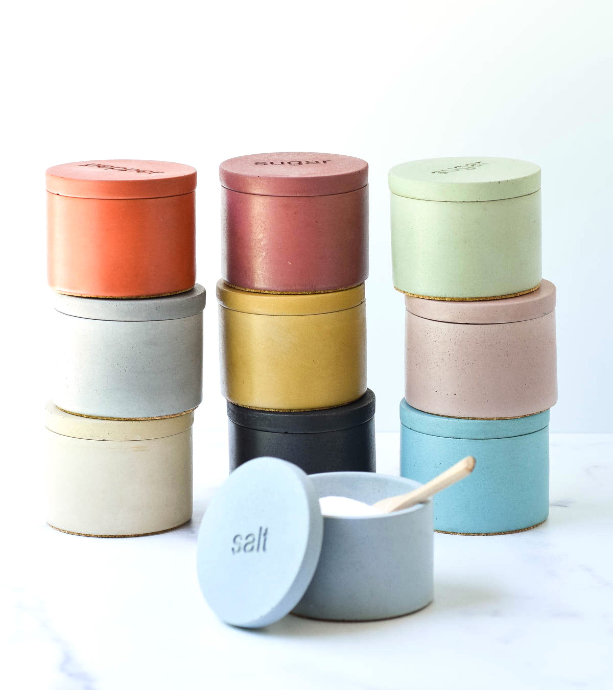 salt, pepper and sugars cellars 3 stacks of 3 various colors one with the lid off and a spoon in the salt
